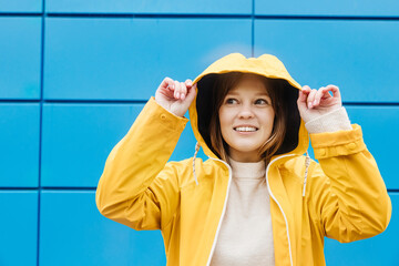 Caucasian girl in yellow raincoat with hood. Young happy beautiful woman wearing rain outfit.
