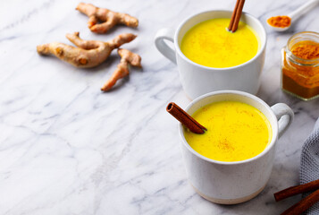 Turmeric tea, latte, golden milk in cups with cinnamon. Marble background. Close up. Copy space.
