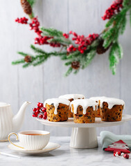 Christmas cakes, puddings on cake stand with cup of tea. Marble table. Grey background.