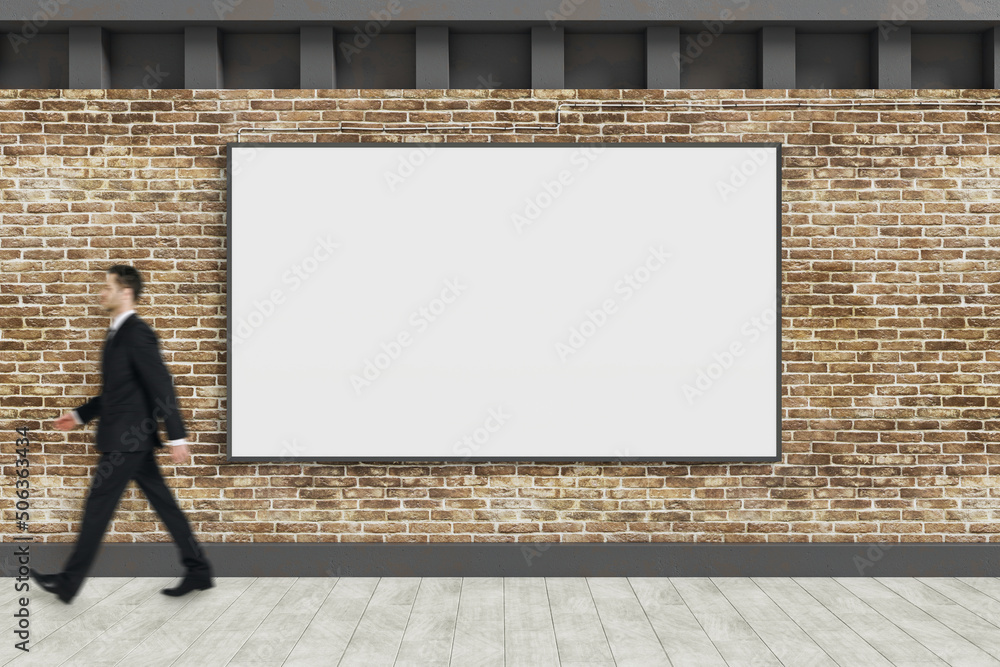 Canvas Prints young businessman walking past empty white banners hanging on brick outdoor wall with shadows and su