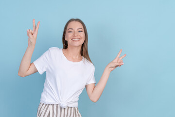 Happy girl dances with happiness making gestures with her hands up in studio on blue background in light casual clothes. Beautiful caucasian young woman posing in the studio on a colored background