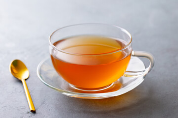 Tea in glass cup with golden spoon. Grey background. Close up.