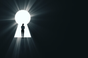 Backlit business woman standing in bright keyhole opening on dark background with mock up place and light rays. Dream, future and opportunity concept.