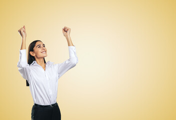 Joyful and satisfied woman in white shirt with raised hands showing her power, winner and achievement concept, isolated on light orange background with empty place for you text or logo, mock up