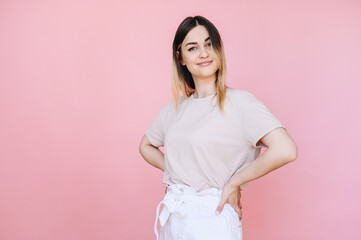Fototapeta premium Portrait of a woman posing on a pink background and holding her hands at her sides.