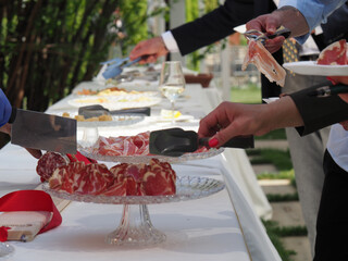 people eating ham and curated meats delicatessen from buffet table at outdoor wedding event