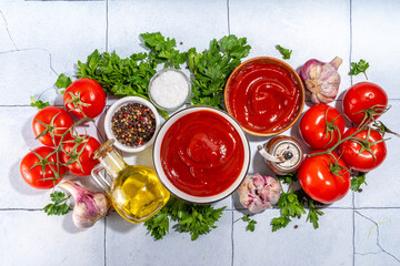 Homemade ketchup sauce. Two bowl with tomato ketchup red sauce with ingredient for cooking - herbs, raw fresh tomatoes, olive oil, garlic, salt, spices, on white tiled background top view copy space