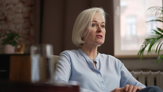 Portrait of elderly female client is visiting psychoanalyst and sitting in chair in office spbas. 4k Close view of beautiful caucasian woman looks with smile and discusses mental problems with