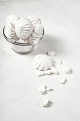 glass vase with meringue stands on a gray background, next to it are a whole and broken dessert of French meringue, a vertical picture.