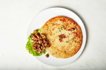 traditional Swiss dish is a potato pancake on a white plate with fried mushrooms and a leaf of green salad, top view.