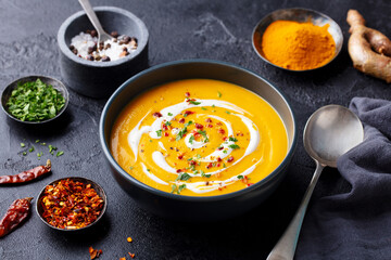 Pumpkin soup with spices in black bowl. Dark background. Close up.