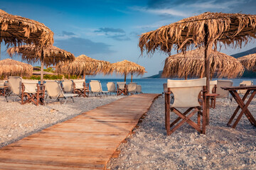 Wonderful summer view of Fokianos beach with wooden pier and straw umbrellas. Adorable  evening scene of Peloponnese peninsula, Greece, Europe. Marvelous summer seascape of Myrtoan Sea.