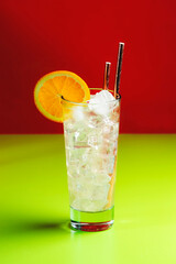Tom Collins popular alcoholic cocktail with dry gin, syrup, lemon juice, soda, orange and ice. Bright red green summer background, negative space