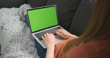 woman lies on a couch and works, prints behind a laptop, a green screen. The concept of work from...