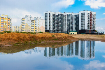 A large puddle after rain at the construction site of a large residential facility. Reflection in the water of the construction site and cranes against the background of the sunset sky.