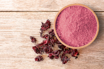 Roselle powder in wooden bowl with dry hibiscus flower isolated on wooden table background.