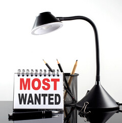 MOST WANTED text on notebook with pen and table lamp on the black background