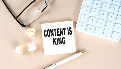 CONTENT IS KING text on sticky with pen ,calculator and glasses on beige background