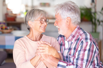 Portrait of lovely elderly couple looking in the eyes hands in hands. Joyful and smiling beautiful senior couple indoors being in great mood