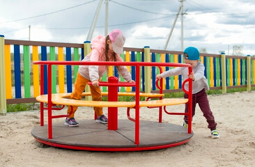Children play in the park on the playground and communicate. Kids are playing a spinning game. Sports, lifestyle and healthy childhood.