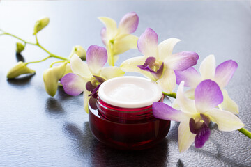 Cymbidium orchid flowers and moisturizer skin care face cream in glass jar isolated on dark...