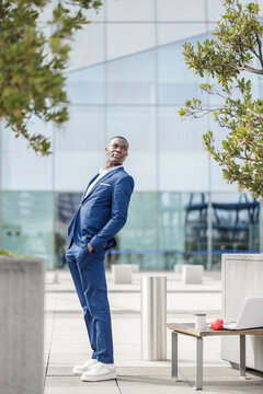 Businessman with hands in pockets leaning backwards on footpath