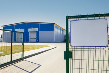 Behind the green fence is a modern industrial building against the blue sky.