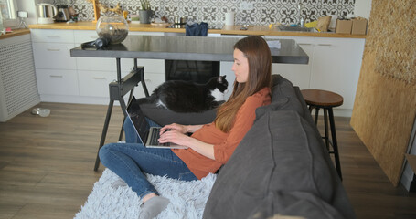 Woman works at home on a laptop, sitting on the couch with a cat. Studying at home, home office, concept.