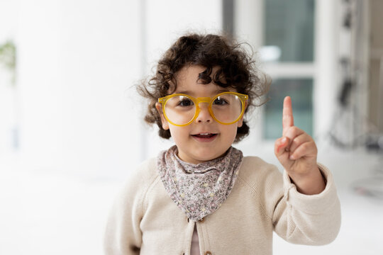 Cute little girl wearing oversized eyeglasses raising finger