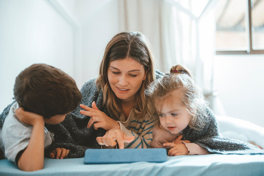 Young woman showing tablet PC to children on bed at home