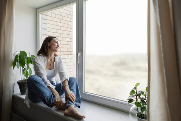 Happy mature woman sitting on window sill at home