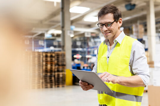 Smiling worker wearing eyeglasses using tablet PC in warehouse
