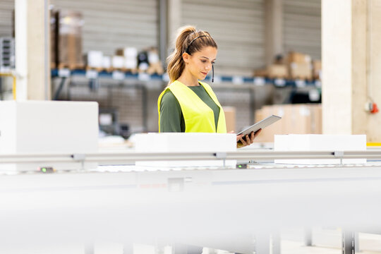 Young worker holding tablet PC analyzing box on conveyor belt in warehouse