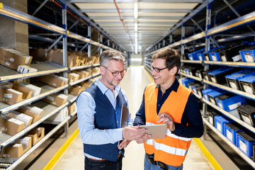 Smiling worker looking at manager discussing over tablet PC in warehouse
