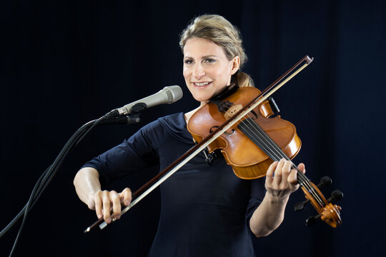 Smiling mature woman playing violin in front of black background