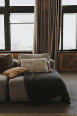 Fototapeta premium Aesthetic modern Scandinavian home interior design. Elegant bohemian living room with comfortable sofa, pillows, windows, curtains, plaid, marble side table