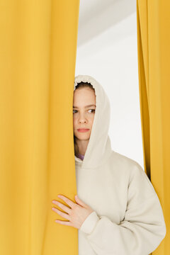 Woman peeking through yellow curtain at home