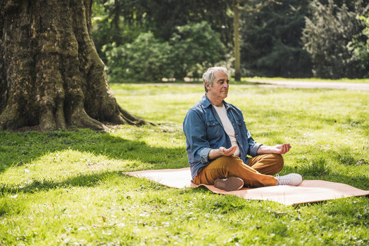 Senior man sitting cross-legged meditating on exercise mat at park
