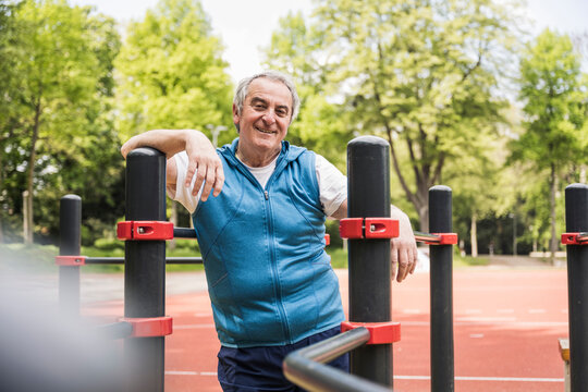 Happy senior man standing amidst gymnastics bar at park