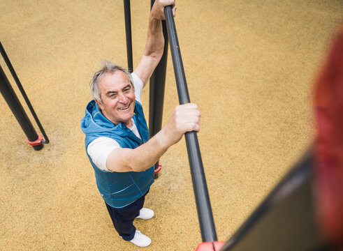 Smiling senior man holding gymnastics bar at park
