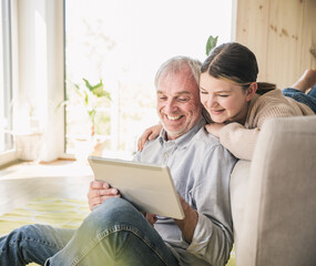 Happy senior man with granddaughter using tablet PC at home