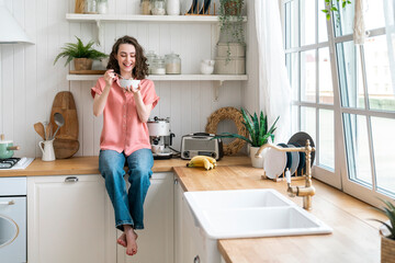 Happy young woman eating breakfast sitting on kitchen counter at home