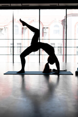 silhouette yogi woman exercising exercising doing Wild Thing, Flip-the-Dog exercise, Camatkarasana pose, exercising in gym on the background of the window, sportswear, healthy lifestyle concept.