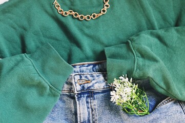 Flat lay photo set new trendy clothes collection. Green sweatshirt, chain, blue jeans and flowers. Stylish clothing top view. Image for design web site, fashion background 
