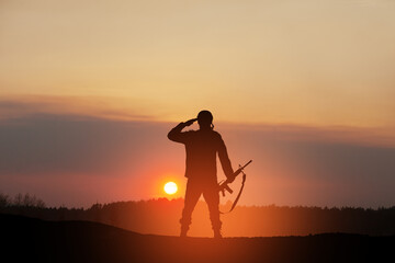 Fototapeta premium Silhouette of soldier standing against the backdrop of a sunset. Greeting card for Veterans Day, Memorial Day, Independence Day. USA celebration. Concept - patriotism, protection, remember honor.