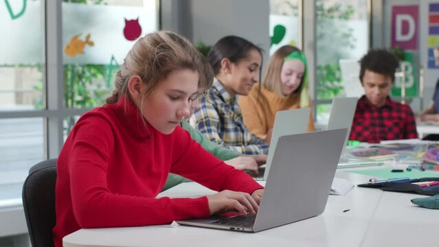 Diverse teen students type on laptop sitting at desk in classroom
