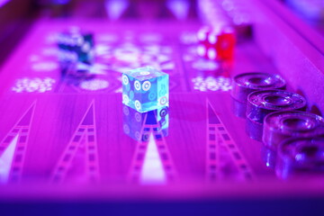 Transparent Blue dice on backgammon board under the purple light.