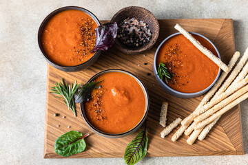 Three bowls of tomato soup or gazpacho with ground pepper, rosemary and bread sticks. Top view.