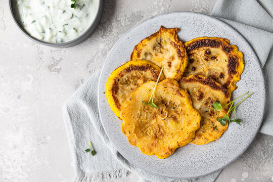 Fried patisson or yellow zucchini with sauce and micro greens, grey background.