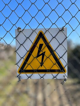 Metal plate representing high voltage warning sign as extra safety measures in industry. Closeup of high voltage warning sign mounted on steel wire mesh against blurry background